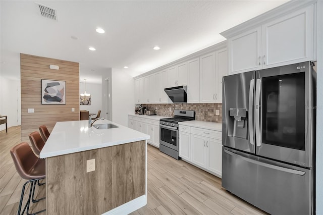 kitchen featuring visible vents, white cabinets, a kitchen island with sink, stainless steel appliances, and light countertops