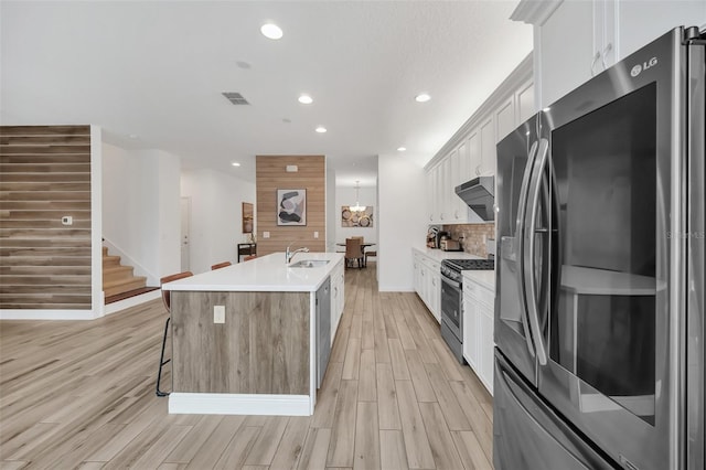 kitchen featuring light countertops, appliances with stainless steel finishes, white cabinets, a sink, and an island with sink