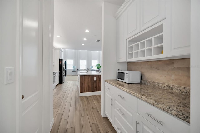 kitchen featuring white cabinets, white microwave, freestanding refrigerator, light stone countertops, and wood finish floors