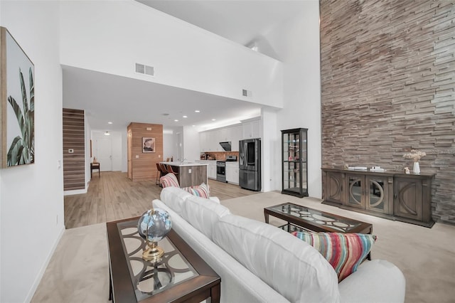 living room with stairs, a high ceiling, visible vents, and light wood-style floors