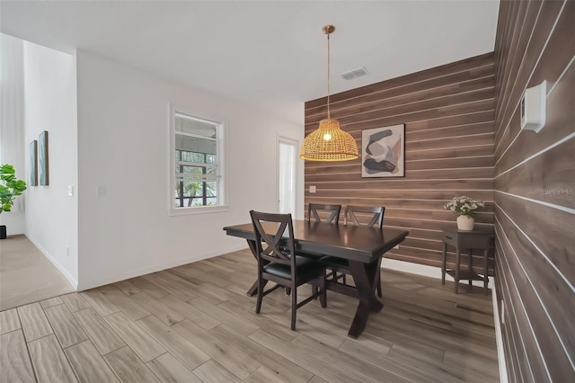 dining space featuring light wood-style floors, baseboards, visible vents, and wood walls