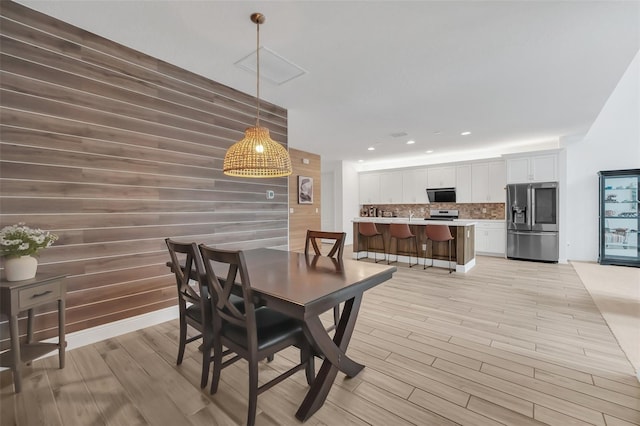 dining space with recessed lighting, wood walls, and light wood finished floors