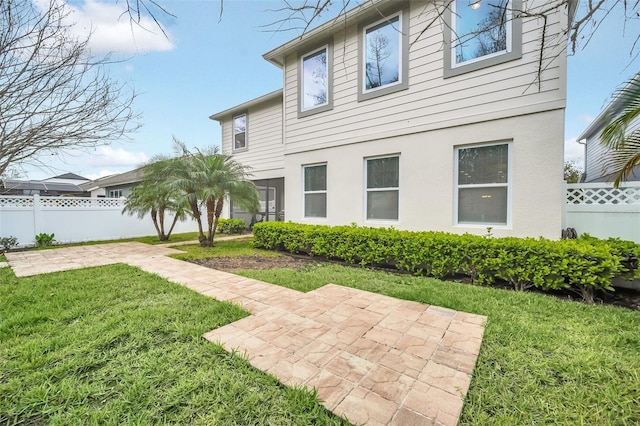 rear view of house with a yard, fence, stucco siding, and a patio