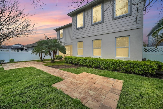 back of property at dusk with a patio area, a yard, fence, and stucco siding