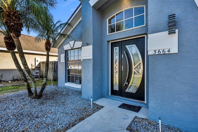 view of exterior entry with fence and stucco siding