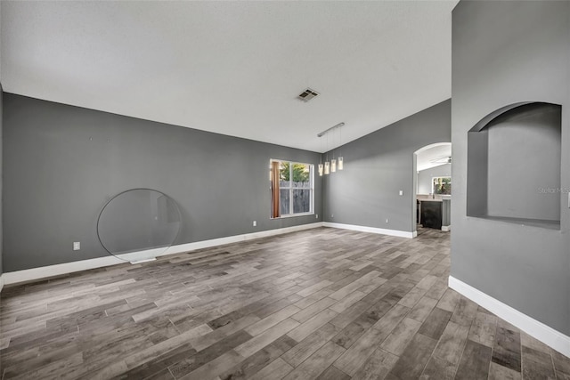 unfurnished living room featuring arched walkways, wood finished floors, visible vents, baseboards, and vaulted ceiling