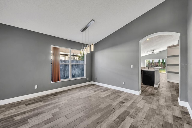 unfurnished dining area with lofted ceiling, arched walkways, a textured ceiling, and wood finished floors