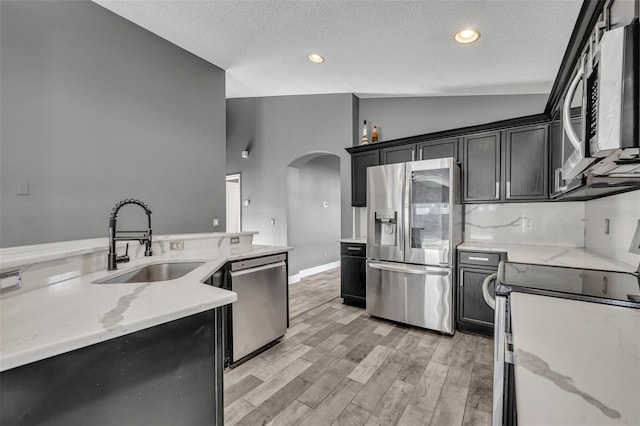 kitchen with arched walkways, lofted ceiling, appliances with stainless steel finishes, dark cabinetry, and a sink