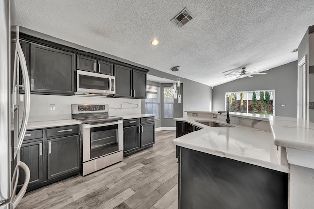 kitchen featuring visible vents, vaulted ceiling, stainless steel appliances, light wood-style floors, and a sink