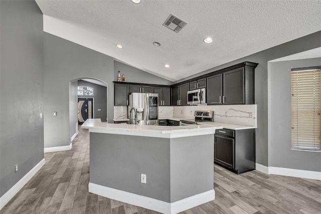 kitchen with arched walkways, stainless steel appliances, visible vents, vaulted ceiling, and an island with sink