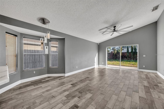 empty room featuring lofted ceiling, visible vents, a ceiling fan, and wood finished floors