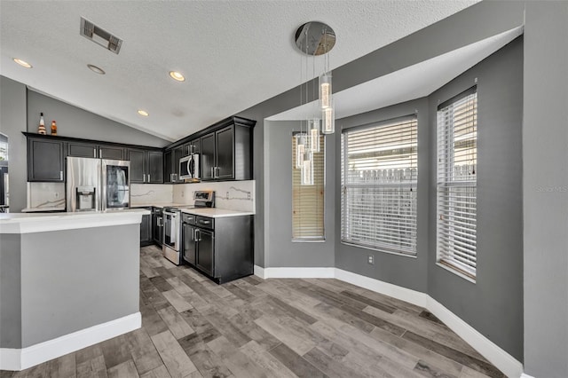 kitchen with lofted ceiling, stainless steel appliances, visible vents, light countertops, and light wood finished floors