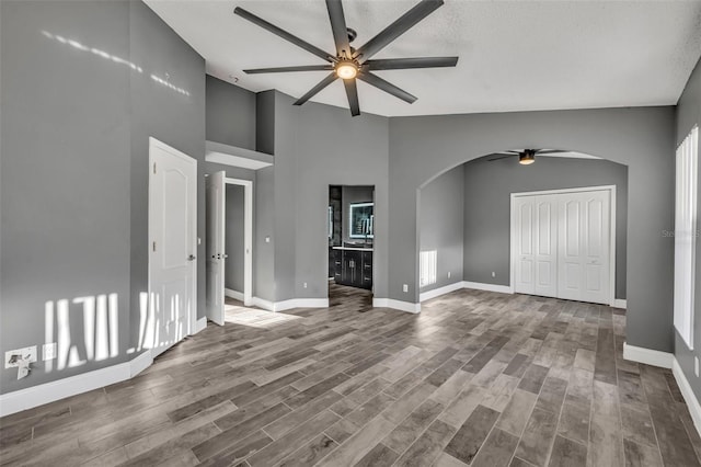 unfurnished living room with arched walkways, wood finished floors, a ceiling fan, and baseboards