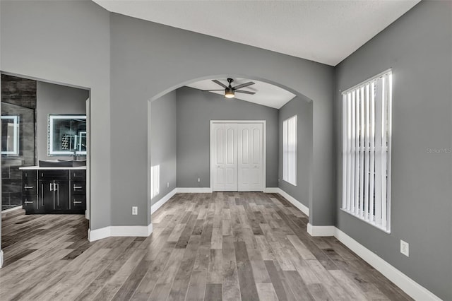 entrance foyer with arched walkways, a ceiling fan, vaulted ceiling, wood finished floors, and baseboards