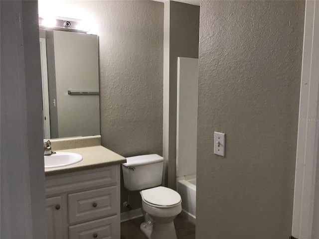 full bathroom with toilet, vanity, and a textured wall