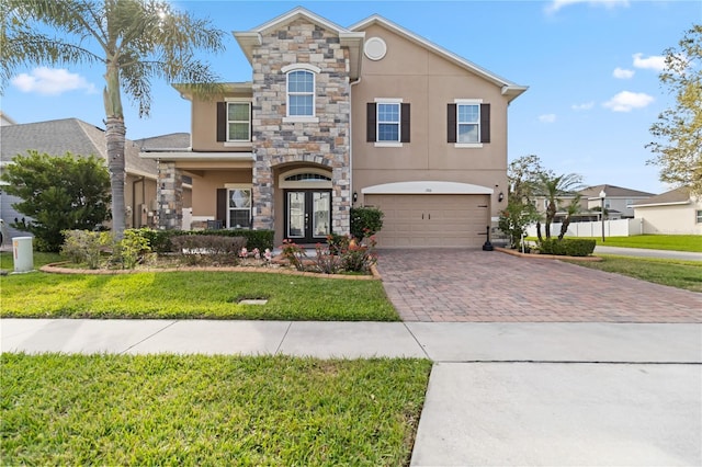 view of front of home with an attached garage, french doors, decorative driveway, stucco siding, and a front lawn