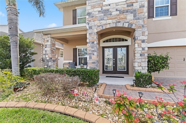 entrance to property with a garage, french doors, stone siding, and stucco siding