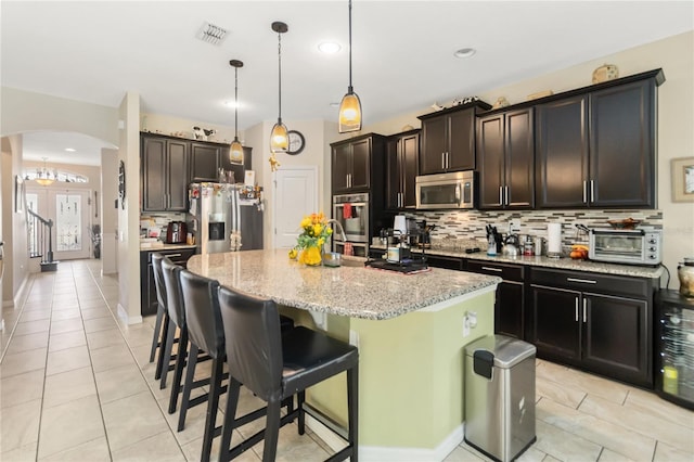 kitchen featuring arched walkways, visible vents, appliances with stainless steel finishes, backsplash, and light stone countertops