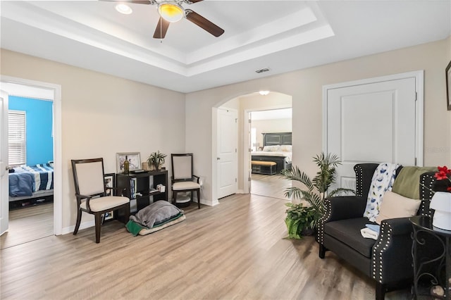 living area with light wood-type flooring, baseboards, arched walkways, and a raised ceiling