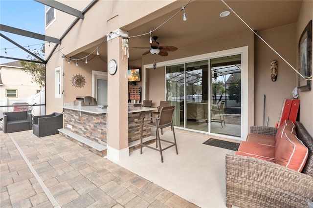 view of patio / terrace featuring glass enclosure, an outdoor kitchen, a ceiling fan, and outdoor wet bar