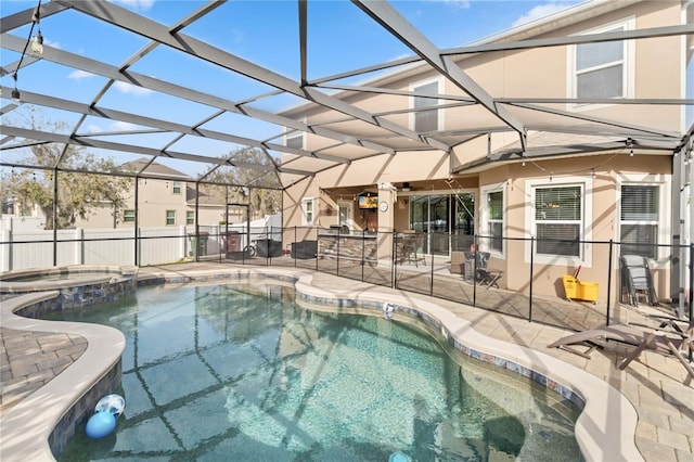 view of swimming pool with a patio area, a pool with connected hot tub, fence, and glass enclosure