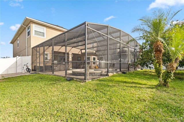 rear view of house featuring stucco siding, a lawn, a patio area, fence, and a lanai