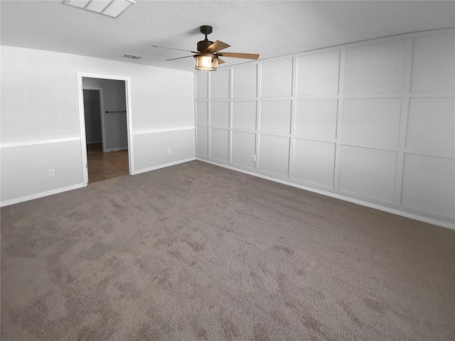 spare room featuring ceiling fan, visible vents, dark colored carpet, and a decorative wall