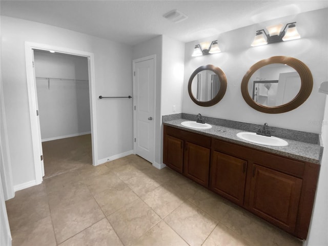 full bathroom with a spacious closet, double vanity, a sink, and visible vents