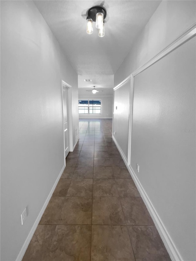 hallway with dark tile patterned flooring and baseboards