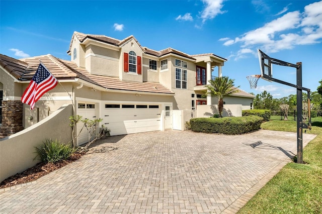 mediterranean / spanish-style house with a tiled roof, an attached garage, fence, decorative driveway, and stucco siding