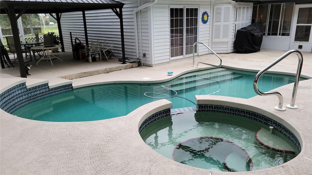 view of swimming pool with a patio, a pool with connected hot tub, and grilling area