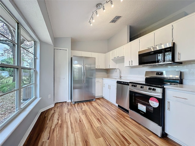 kitchen with tasteful backsplash, appliances with stainless steel finishes, white cabinets, and light countertops