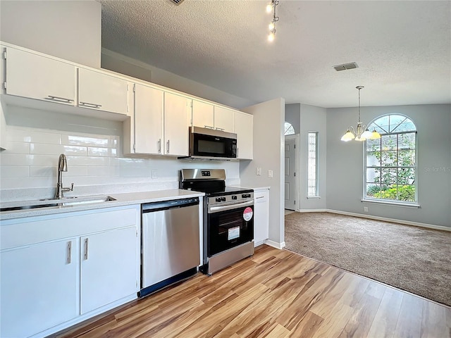 kitchen featuring appliances with stainless steel finishes, pendant lighting, white cabinetry, and a sink