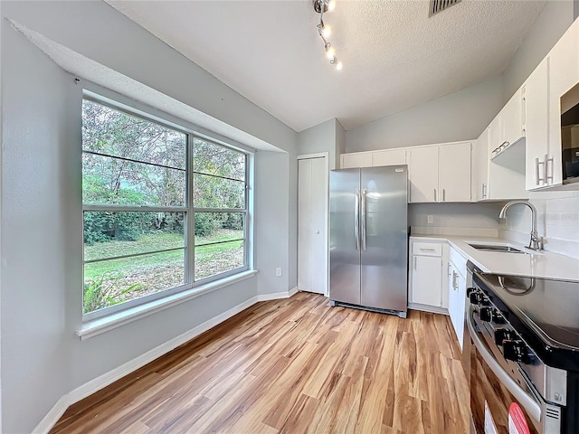 kitchen with stainless steel appliances, light countertops, white cabinets, vaulted ceiling, and a sink