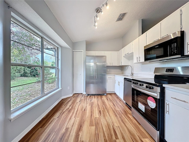 kitchen featuring stainless steel appliances, visible vents, white cabinetry, vaulted ceiling, and light countertops