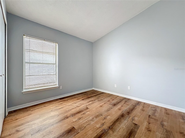 empty room featuring baseboards, lofted ceiling, and light wood-style floors