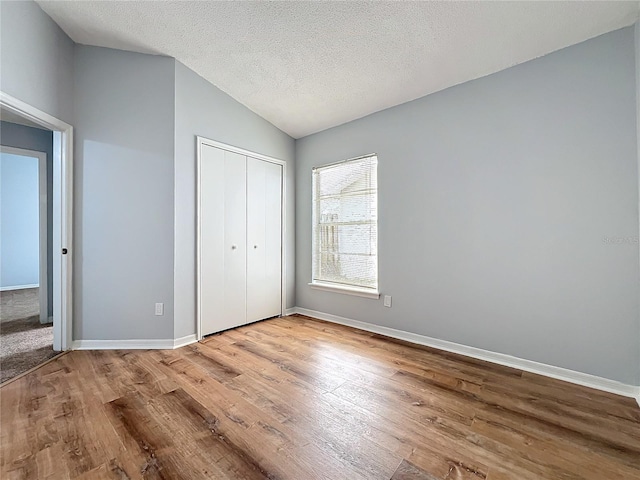 unfurnished bedroom with baseboards, lofted ceiling, light wood-style flooring, a textured ceiling, and a closet