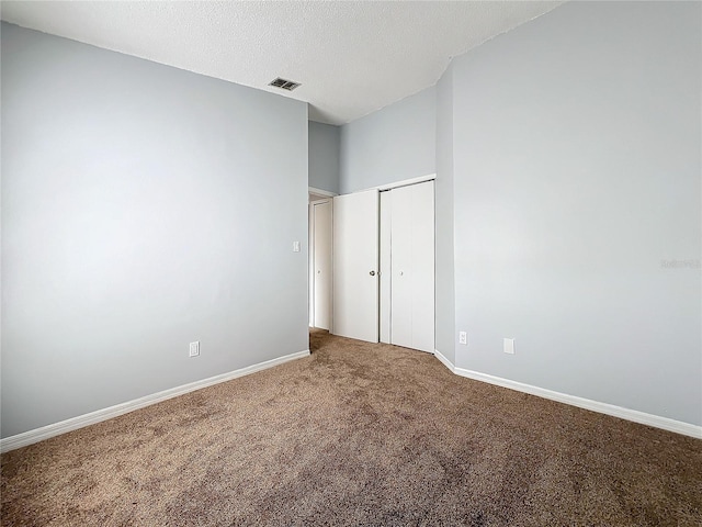 unfurnished bedroom with a textured ceiling, carpet flooring, visible vents, and baseboards