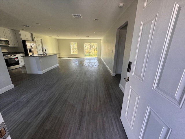 kitchen featuring stainless steel appliances, visible vents, white cabinetry, open floor plan, and an island with sink