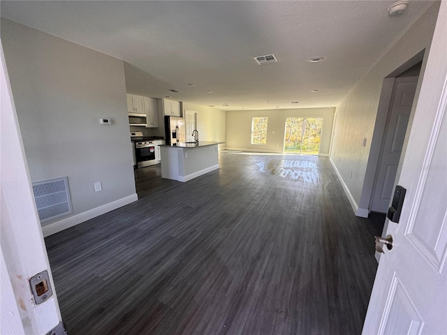 unfurnished living room with dark wood-type flooring, a sink, visible vents, and baseboards