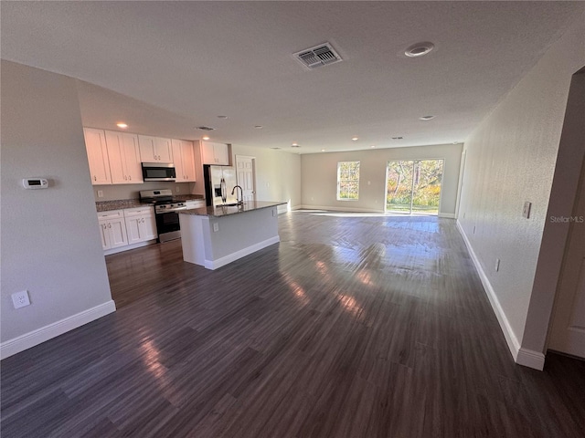 kitchen with visible vents, an island with sink, open floor plan, stainless steel appliances, and white cabinetry