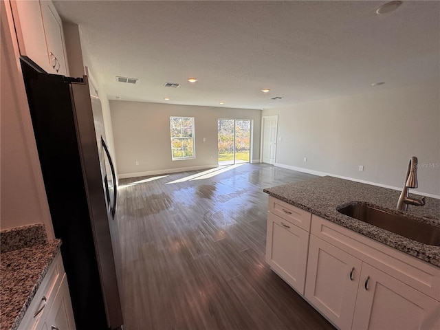 kitchen featuring a sink, white cabinetry, open floor plan, freestanding refrigerator, and dark stone counters