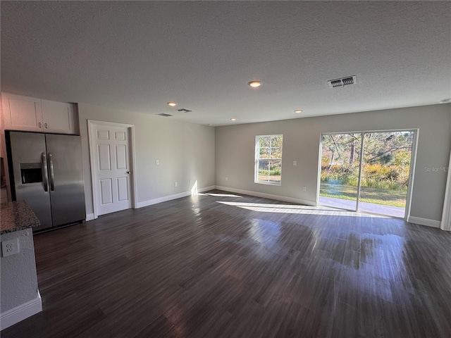 unfurnished living room with a textured ceiling, dark wood finished floors, visible vents, and baseboards