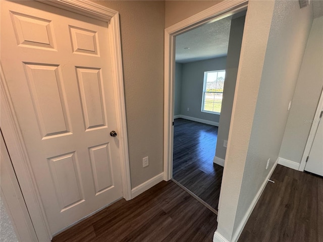 corridor with a textured ceiling, baseboards, and dark wood-style flooring