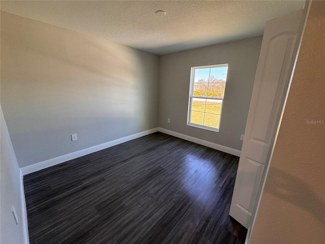 unfurnished room featuring a textured ceiling, dark wood finished floors, and baseboards