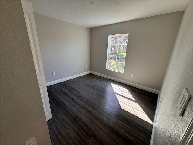 spare room with a textured ceiling, dark wood-type flooring, and baseboards