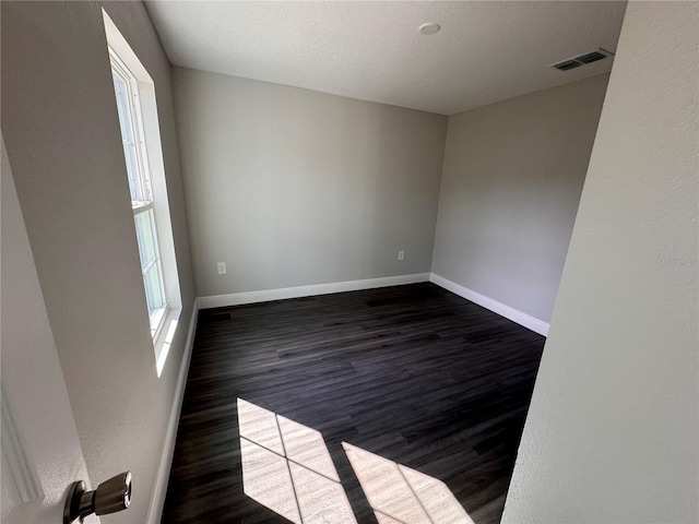 empty room featuring dark wood-style floors, plenty of natural light, visible vents, and baseboards