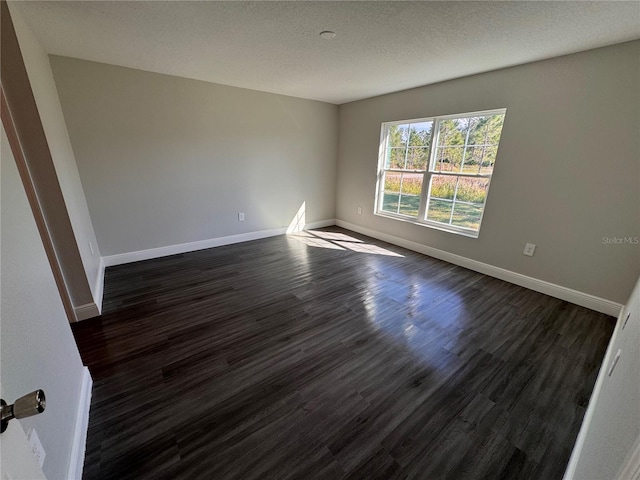 empty room with a textured ceiling, baseboards, and dark wood-type flooring