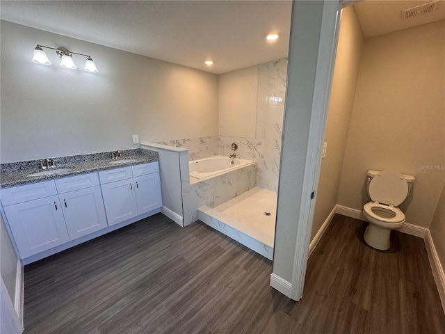 bathroom featuring a garden tub, wood finished floors, a sink, and toilet