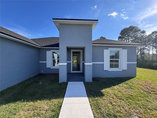 doorway to property featuring a yard, a shingled roof, and stucco siding